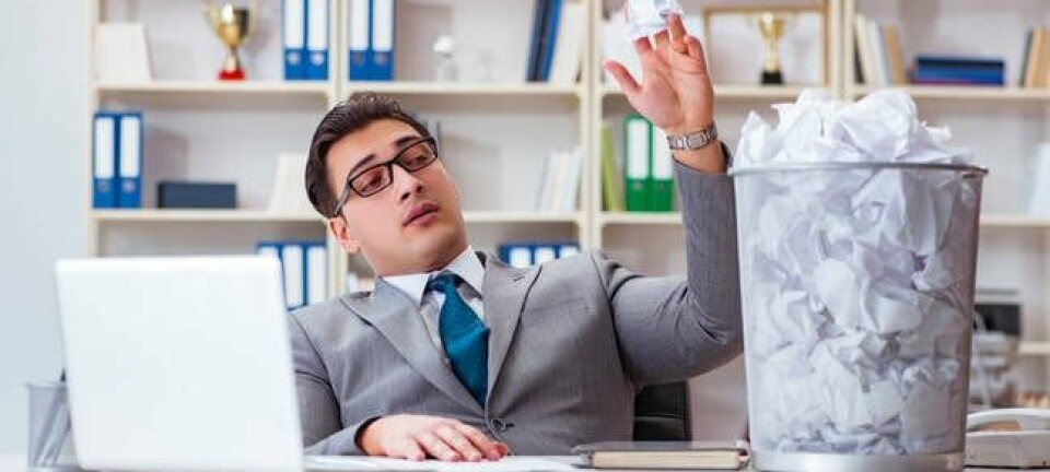 Man in office flippantly throws balls of paper in bin
