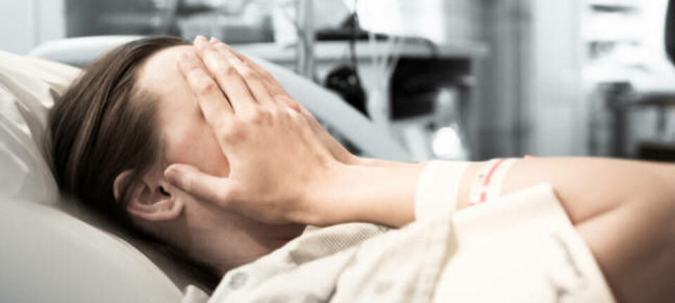 Woman in hospital (in hospital gown) covers face with hands
