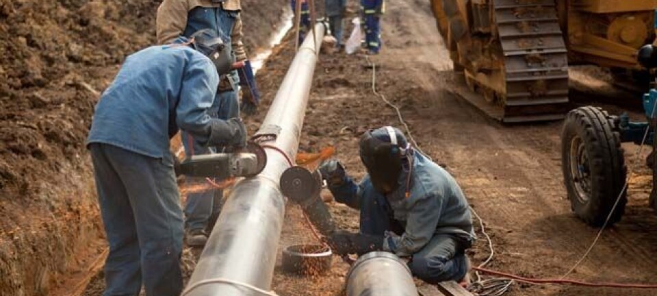 Welders wearing protective clothing fixing welding and grinding industrial construction oil and gas or water and sewerage plumbing pipeline outside on site. Photo by Andrea Slatter/Shutterstock