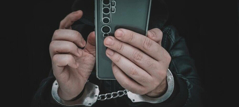 Photo of a scammer in cuffs holding a phone