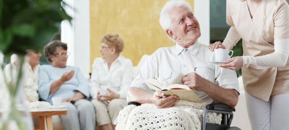 Smiling elder man on wheelchair with braided blanket on legs and reads book