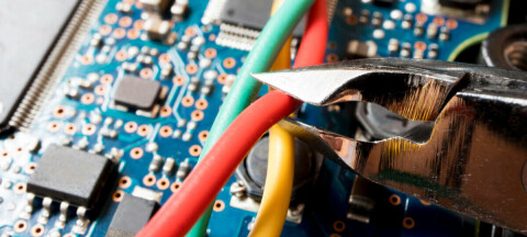 Wire cutters cutting a red wire over a circuit board