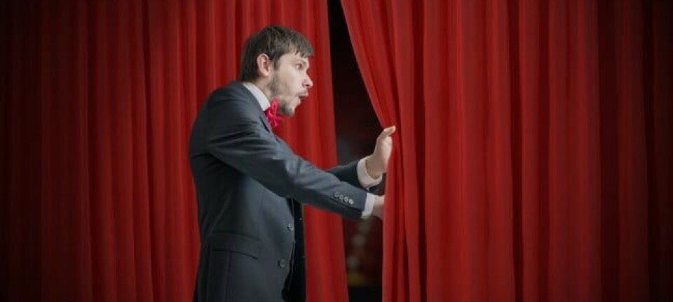Curious actor or illusionist is looking behind red curtain