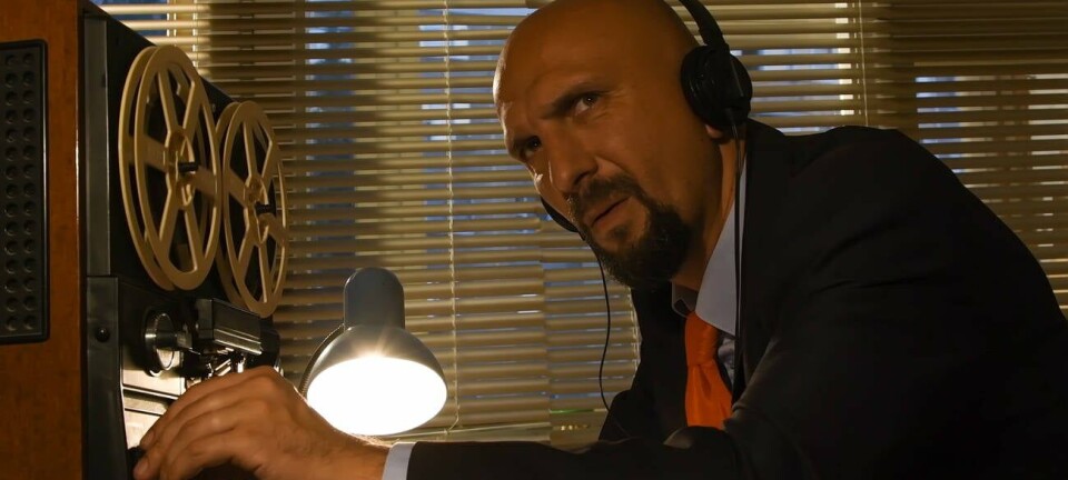 spy in a suit and tie with headphones  listens to audio recorded by bug on a giant tape player...