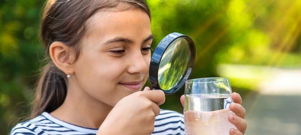 Girl looking at a glass of water through a magnifying glass