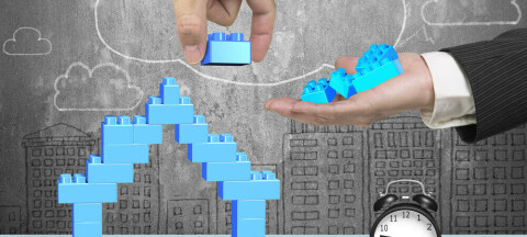 Hands removing blocks from a blue Lego house in front of a cloud drawing on a chalkboard