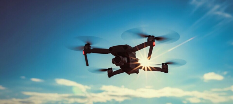 A quadcopter drone flies against a blue sky with scattered clouds.