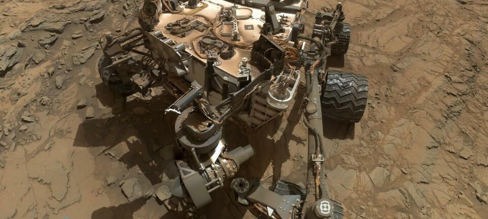 A NASA Curiosity rover sits on a rocky Mars landscape with its robotic arm extended.