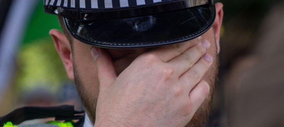 Close-up of a police officer in a checkered cap covering their face with one hand.